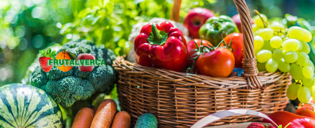 Cesto de verga com fruta e legumes. Por exemplo, uvas brancas, pimentos, tomates, brócolos, cenouras